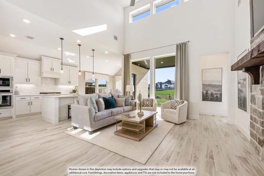 Open-concept living room with two-story ceiling, light wood floors, and adjoining white kitchen with island Open-concept living room with two-story ceiling, light wood floors, and adjoining white kitchen with island