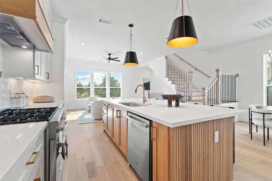 A large island with a built-in sink accented by premium Moen fixtures, sleek stainless steel appliances, and a seamless flow into the living area - perfect for both everyday living and entertaining.