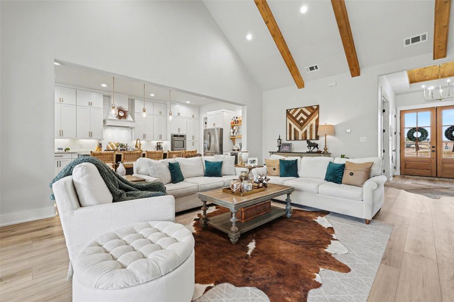 Living room with LVP floors, high vaulted ceiling, recessed lighting, remote ceiling fan and beam ceiling