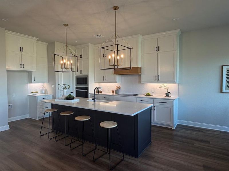 Two tone kitchen with a breakfast bar area, a kitchen island with sink, dark wood-type flooring, stainless steel appliances, and a chandelier