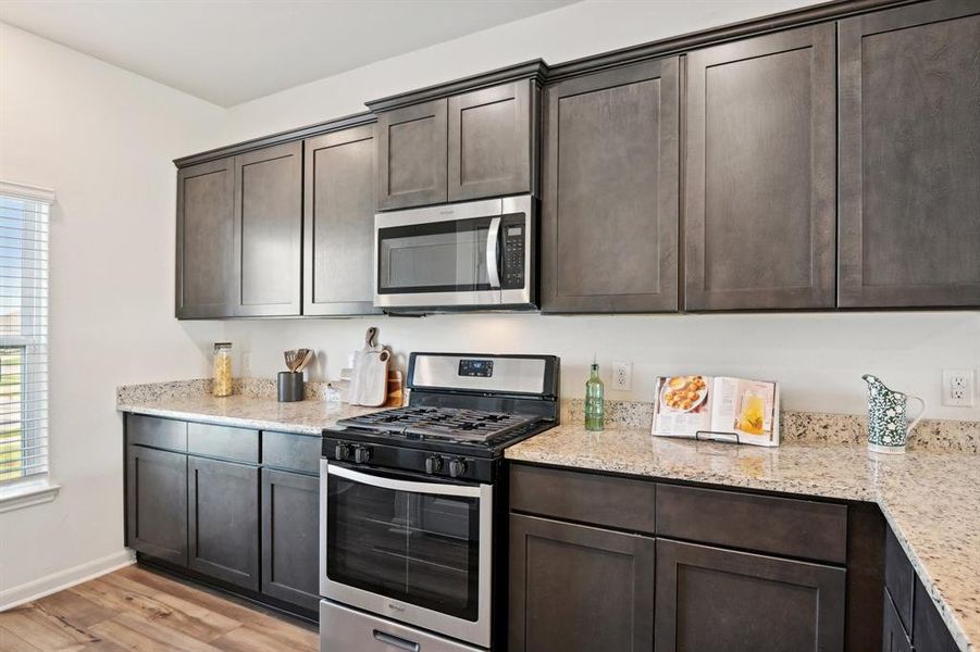 Kitchen with light hardwood / wood-style flooring, stainless steel appliances, light stone counters, and dark brown cabinets