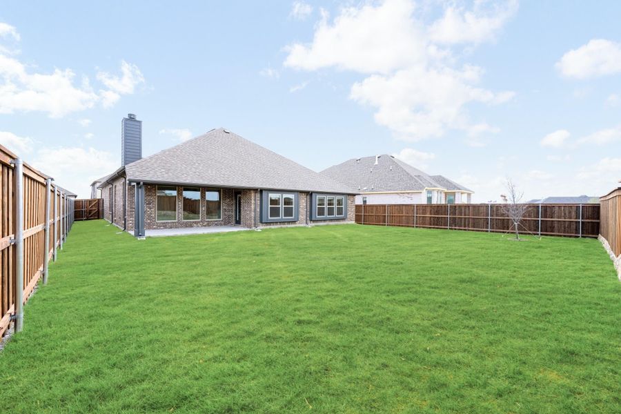 Backyard of brick home with large green lawn, wood privacy fence, and covered patio