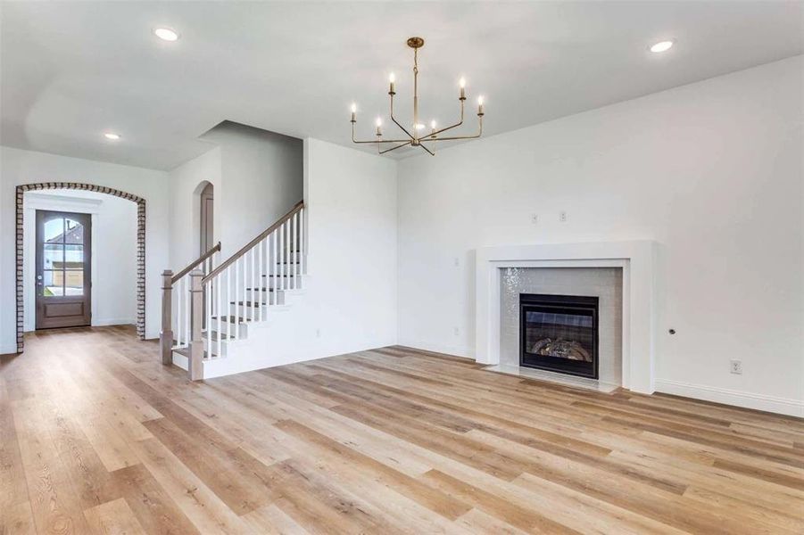 Unfurnished living room with recessed lighting, light wood-style flooring, stairway, a tiled fireplace, and arched walkways Unfurnished living room with recessed lighting, light wood-style flooring, stairway, a tiled fireplace, and arched walkways