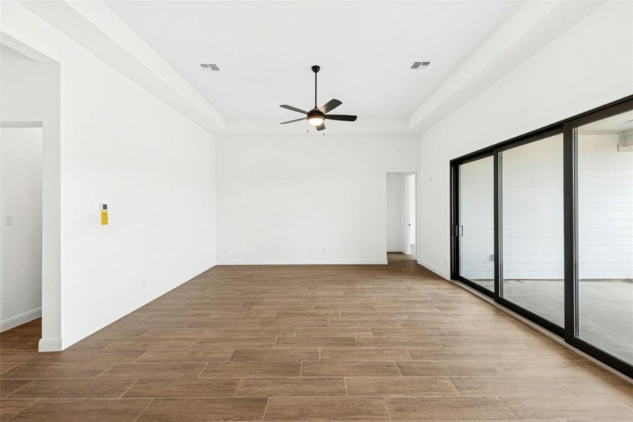 Unfurnished bedroom with wood finish floors, access to outside, a raised ceiling, and ceiling fan