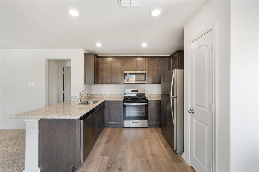 Kitchen featuring light wood-style flooring, light stone counters, stainless steel appliances, sink, and kitchen peninsula