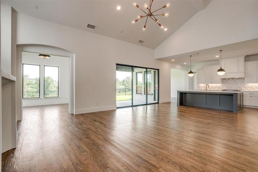 Unfurnished living room featuring high vaulted ceiling, wood-type flooring, sink, and a chandelier