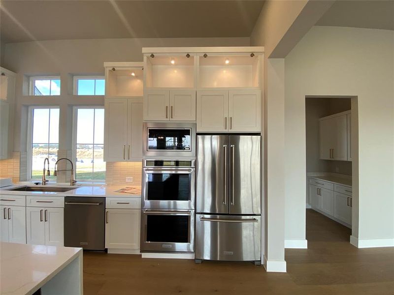Kitchen with appliances with stainless steel finishes, white cabinets, light stone countertops, tasteful backsplash, and dark wood-style flooring