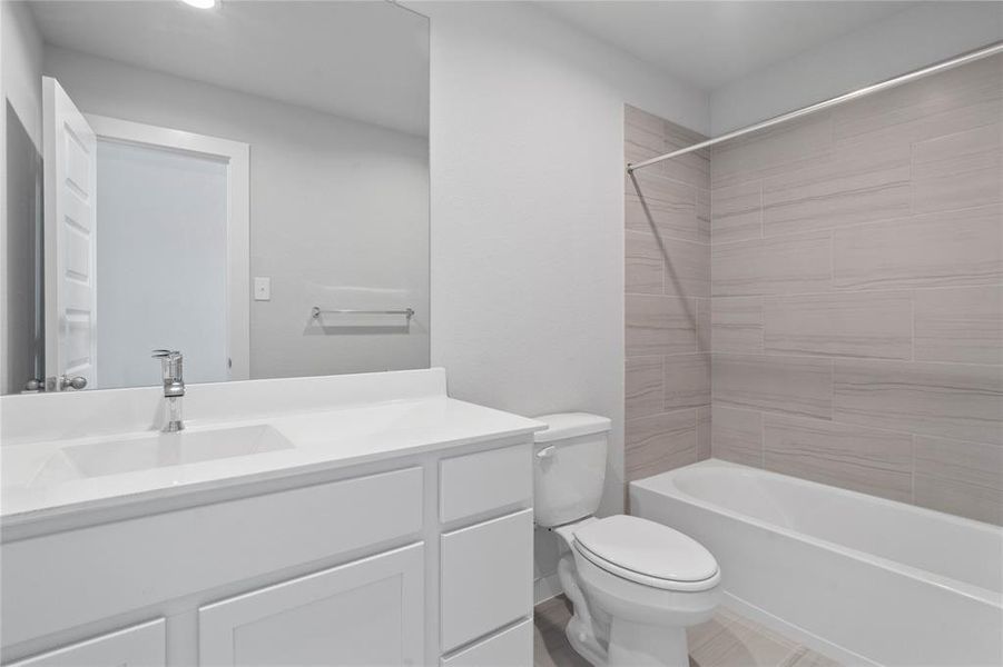 Secondary bath features tile flooring, bath/shower combo with tile surround, stained wood cabinets, beautiful light countertops, mirror, sleek fixtures and modern finishes.