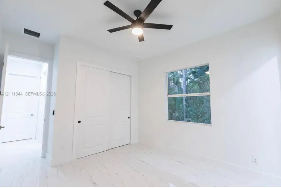 Neutral-toned room featuring light-colored flooring with marble-finish detailing, a ceiling fan with integrated lighting, and a dual-panel sliding closet door Neutral-toned room featuring light-colored flooring with marble-finish detailing, a ceiling fan with integrated lighting, and a dual-panel sliding closet door