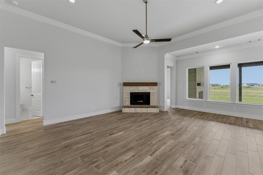Spacious living area featuring wood-finish flooring, a corner fireplace with a stone surround and wood mantel, crown molding, and recessed lighting