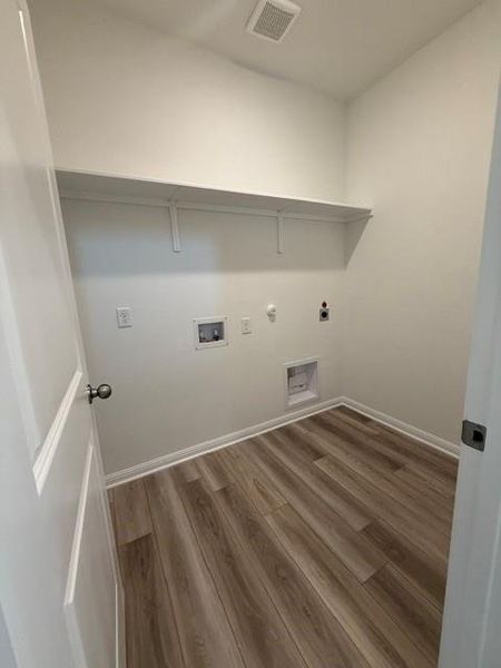 Dedicated laundry area featuring wood-finish flooring, crisp white walls, built-in shelving, and utility hookups
