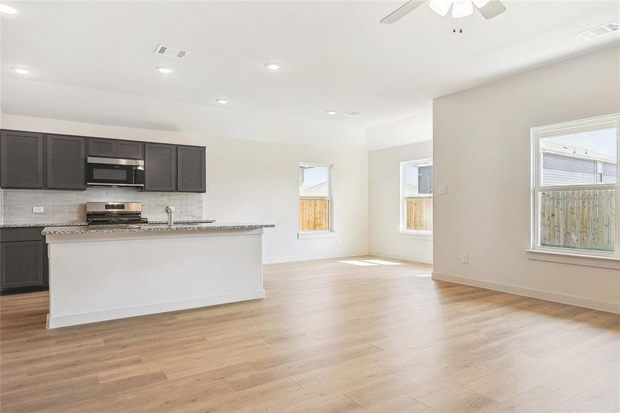 Kitchen featuring light wood-type flooring, ceiling fan, tasteful backsplash, light stone counters, and appliances with stainless steel finishes