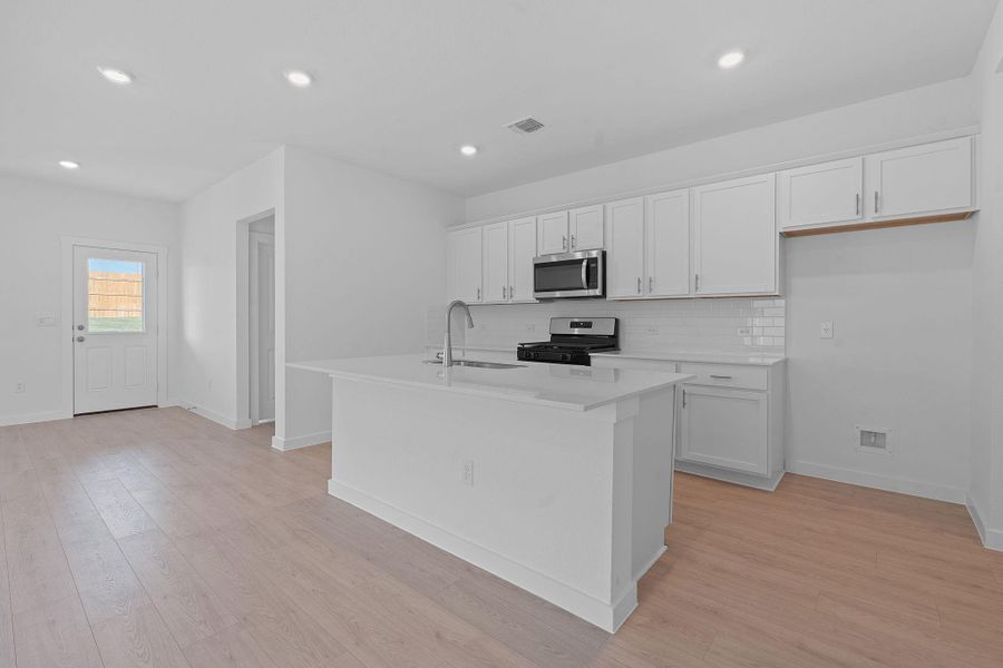 Kitchen with white cabinetry, backsplash, stainless steel appliances, light wood-style flooring, and recessed lighting