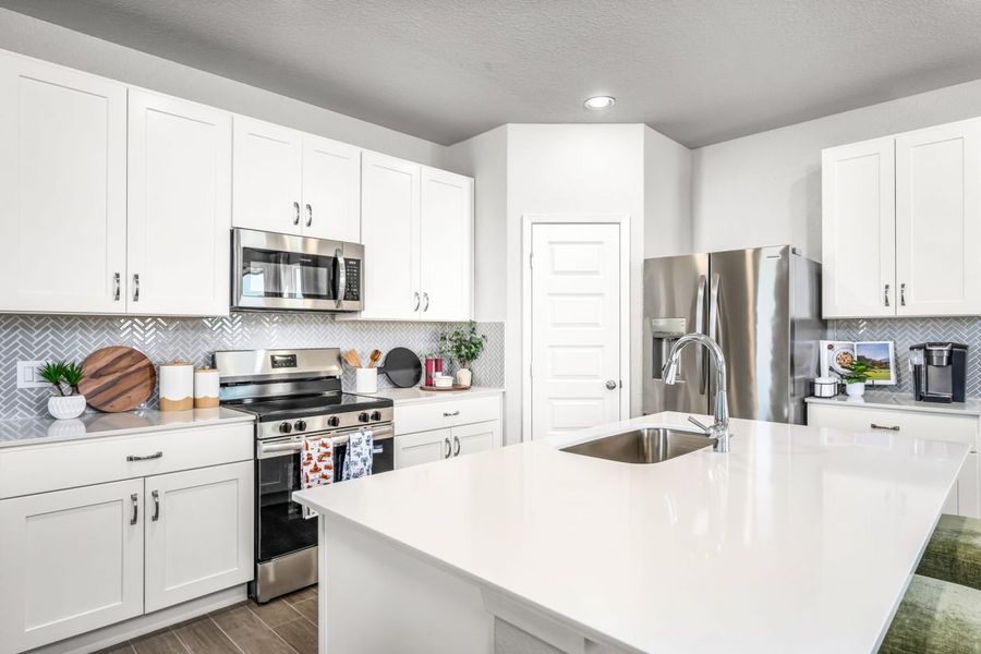 Image of kitchen with white cabinets with white countertops, wood flooring, and a white painted wall.