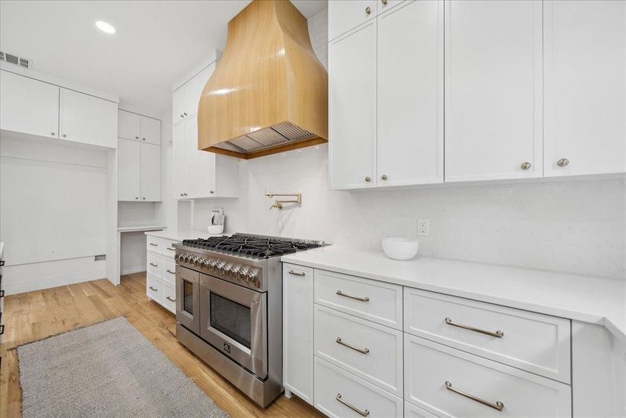 Kitchen with white cabinetry, custom exhaust hood, and double oven range