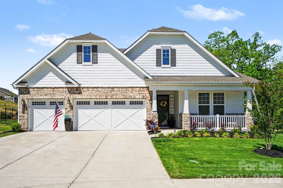 Beautiful home with inviting curb appeal, showcasing a blend of brick and siding, a welcoming covered front porch, and professionally landscaped grounds with a lush lawn and manicured shrubs. Warm exterior lighting and charming architectural details enhance its overall appeal.