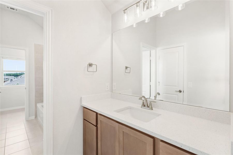 Bathroom vanity with wood cabinets, quartz countertop, single sink, and large mirror with overhead lighting