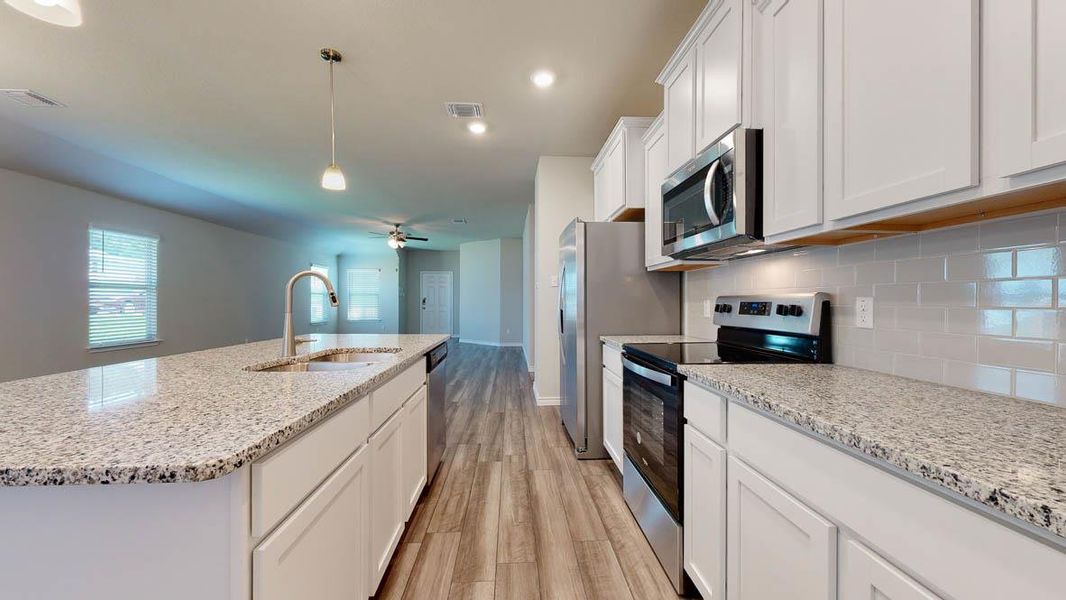 Kitchen featuring a large island with an undermount sink, stainless steel appliances, white cabinetry, and light-toned countertops