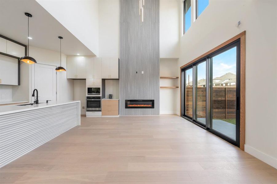 Unfurnished living room featuring light wood finished floors, a large fireplace, and a high ceiling Unfurnished living room featuring light wood finished floors, a large fireplace, and a high ceiling