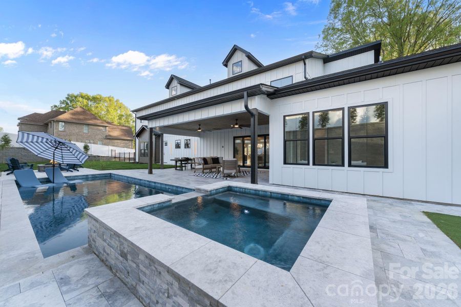 Heated pool with tanning deck, accent lighting, and surrounded by a Travertine deck and patio
