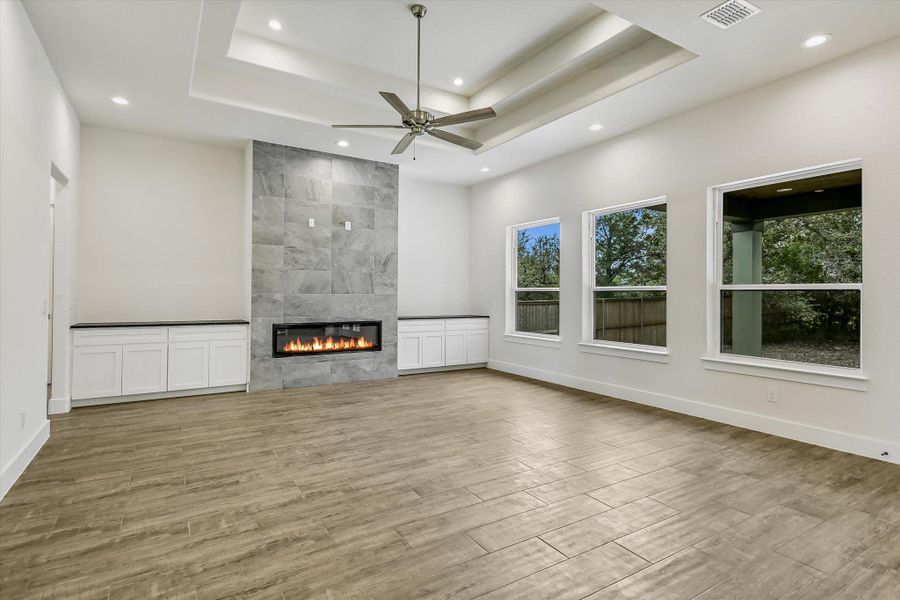 Unfurnished living room with ceiling fan, a tile fireplace, light wood-style floors, recessed lighting, and a raised ceiling