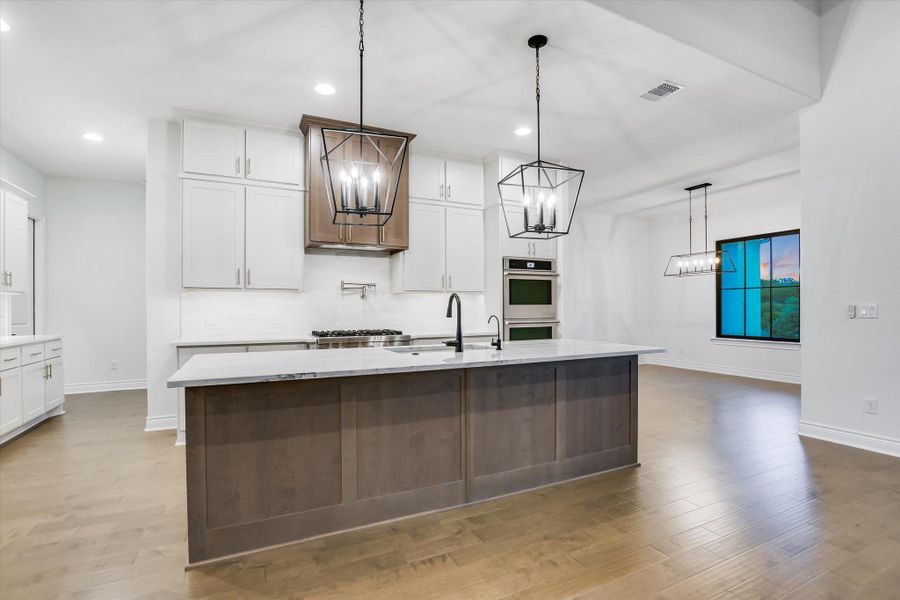 Kitchen with a chandelier, appliances with stainless steel finishes, recessed lighting, white cabinets, and an island with sink