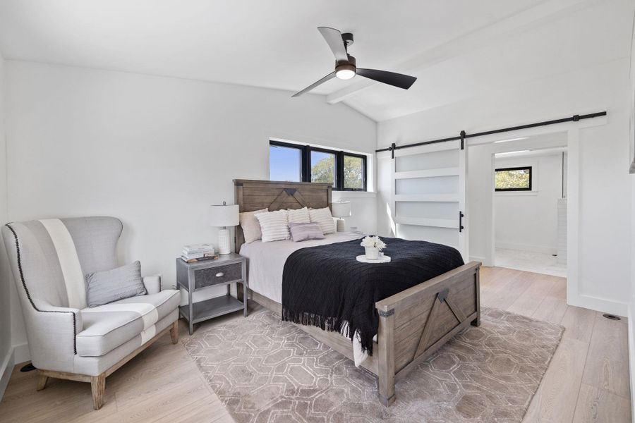 Bedroom featuring light wood-type flooring, multiple windows, a barn door, and a ceiling fan