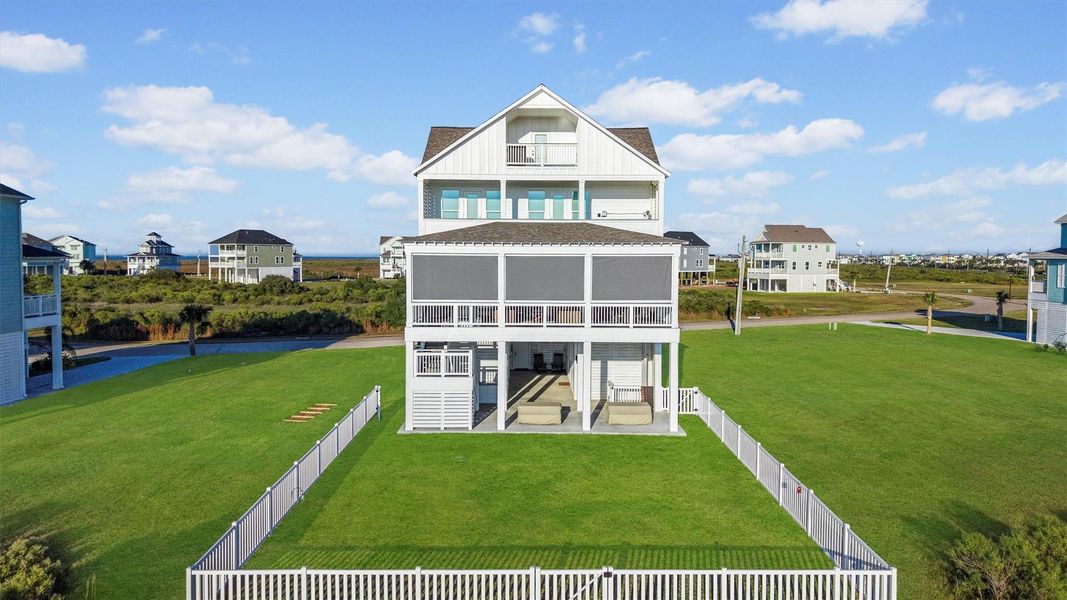 Spacious coastal home with three stories, featuring a 38' x 22' first floor balcony with motorized  screens overlooking the fenced back yard. The property offers expansive green space and scenic views, ideal for enjoying outdoor living.