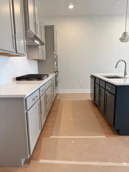 Kitchen featuring backsplash, cooktop, dishwashing machine, range hood, and a sink