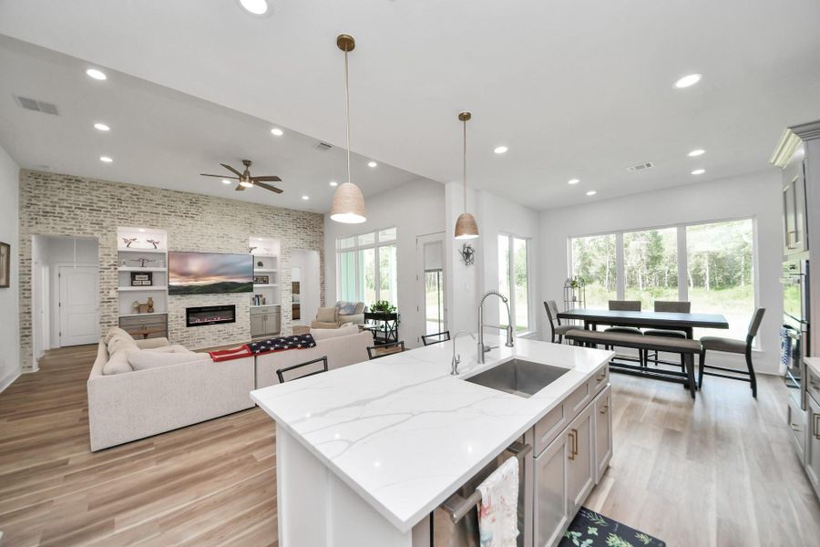 Spacious open-concept living area with modern kitchen, large island, cozy brick accent wall, and expansive windows offering serene views. Spacious open-concept living area with modern kitchen, large island, cozy brick accent wall, and expansive windows offering serene views.