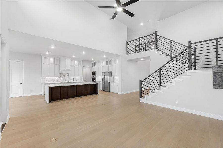 Open living area with high ceilings, hardwood floors, white kitchen, dark island, and staircase with metal railing