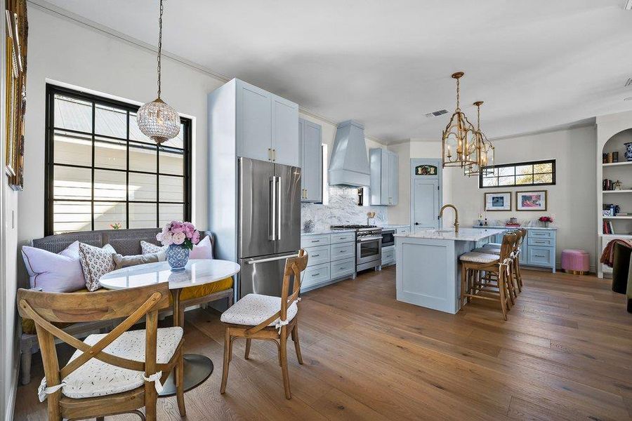 Kitchen with high end appliances, a kitchen breakfast bar, dark wood-style floors, hanging lights, and an island with sink