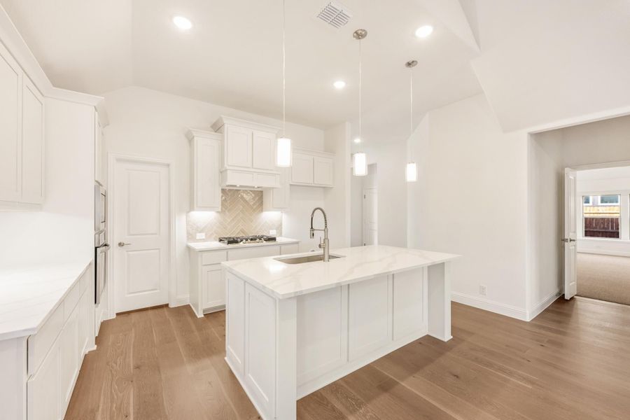 White kitchen with center island, pendant lights, herringbone backsplash, and hardwood floors White kitchen with center island, pendant lights, herringbone backsplash, and hardwood floors