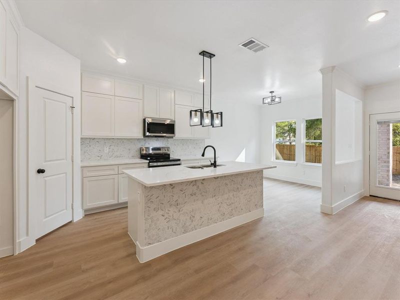 Kitchen featuring decorative backsplash, a kitchen island with sink, pendant lighting, white cabinets, and recessed lighting