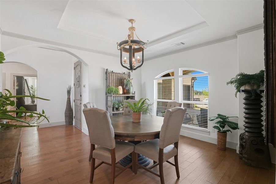 Dining area with a tray ceiling, wood-type flooring, arched walkways, and crown molding Dining area with a tray ceiling, wood-type flooring, arched walkways, and crown molding