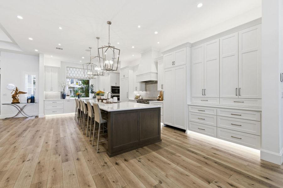 Kitchen with two tone cabinets, a kitchen breakfast bar, a spacious island, hanging lights, and light wood-style floors