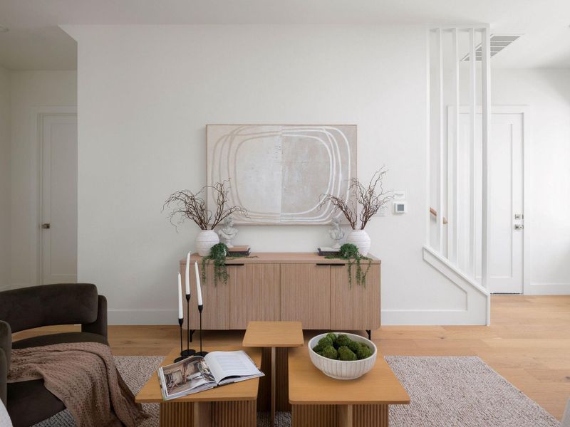 Blonde wood flooring unifies this open-concept living space, leading to a contemporary stairwell with sleek vertical railings.