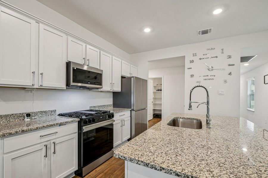 Kitchen featuring stainless steel appliances, white cabinets, light stone counters, dark wood-style floors, and a kitchen island with sink