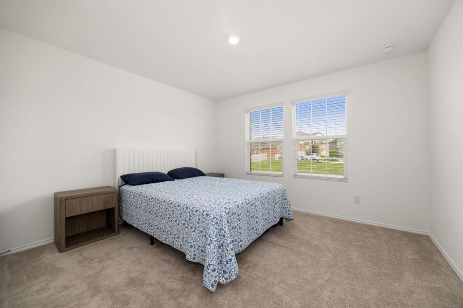 A well-lit bedroom features plush carpeting and broad windows.