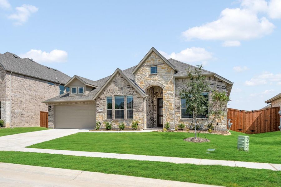 Single-story home with stone and brick exterior, arched entry, two-car garage, and green front lawn