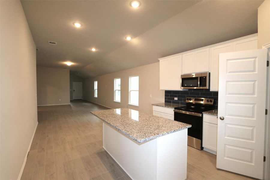 Kitchen featuring appliances with stainless steel finishes, backsplash, lofted ceiling, white cabinets, and a center island