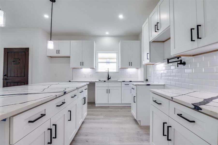Kitchen featuring light stone counters, light wood-style flooring, white cabinetry, decorative light fixtures, and backsplash Kitchen featuring light stone counters, light wood-style flooring, white cabinetry, decorative light fixtures, and backsplash