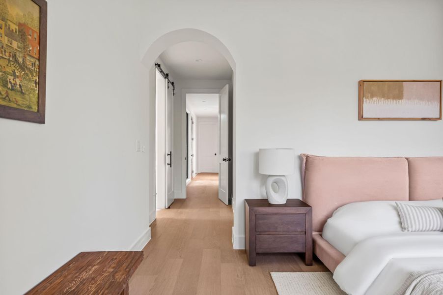 Blonde hardwood floors stretch through an arched entryway leading to a private hall.