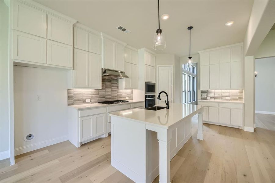 Kitchen with light hardwood / wood-style floors, tasteful backsplash, and ventilation hood