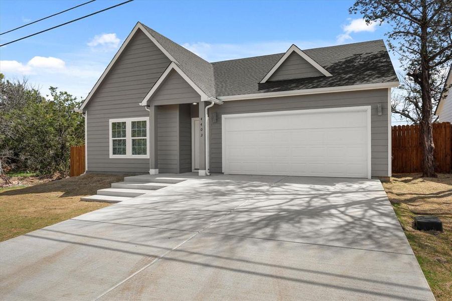 View of front facade with a garage, roof with shingles, concrete driveway, and fence