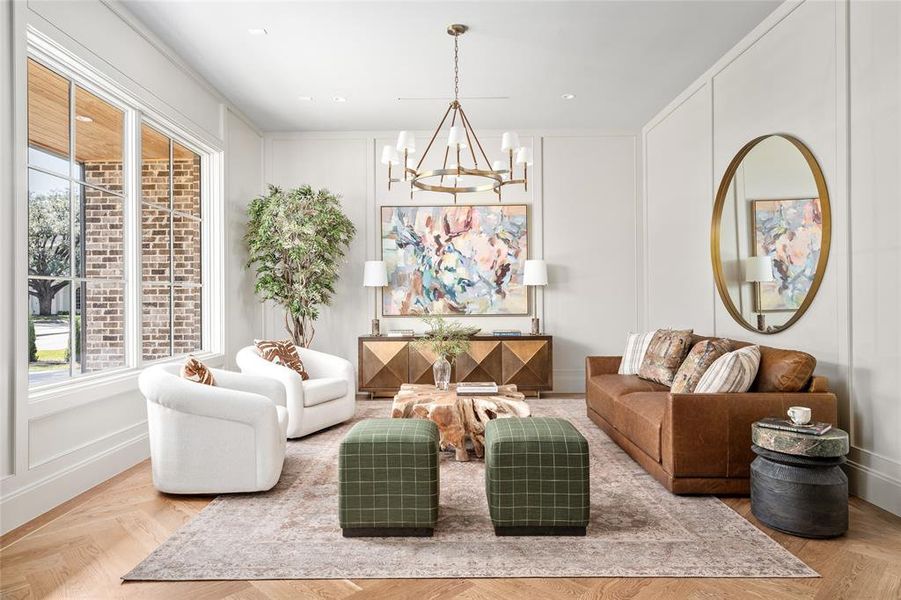 Exuding timeless elegance, this formal living room is anchored by a striking Ralph Lauren Katie chandelier that casts a warm, inviting glow. Refined wall paneling adds depth and sophistication, while a large picture window floods the space with natural light. The herringbone white oak hardwood floors with a brass inlay border complete the room with a touch of luxury.