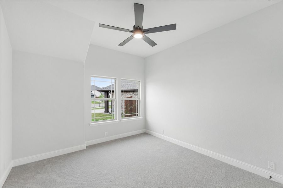 Empty bedroom with gray carpet, ceiling fan, vaulted ceiling, and double windows overlooking neighborhood Empty bedroom with gray carpet, ceiling fan, vaulted ceiling, and double windows overlooking neighborhood