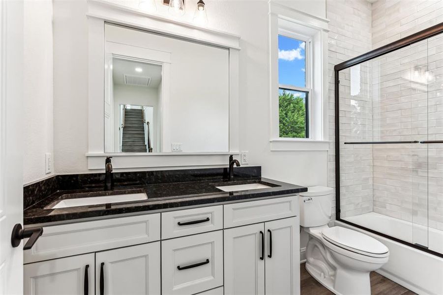 Full guest bathroom with double vanity, toilet, tiled shower over tub with glass door