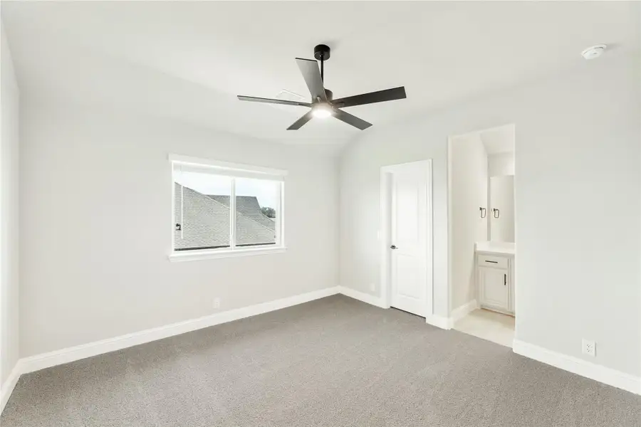 Empty bedroom with gray carpet, black ceiling fan, and ensuite bathroom entrance Empty bedroom with gray carpet, black ceiling fan, and ensuite bathroom entrance
