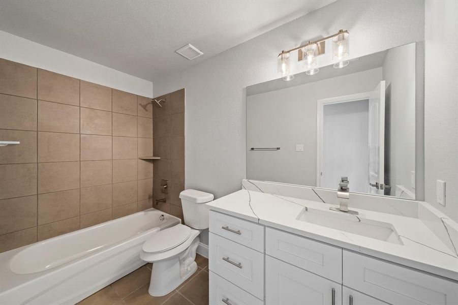 Full bathroom with vanity, tile patterned flooring, tiled shower / bath combo, and toilet